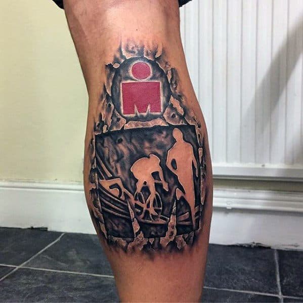 Tattoo featuring the Ironman logo breaking through the skin, with silhouettes of a cyclist, runner, and swimmer representing the full Ironman race.