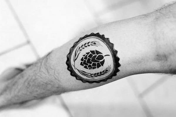 Blackwork tattoo of a hop cone and wheat stalks inside a bottle cap design, symbolizing craft beer culture with clean lines and bold contrast.
