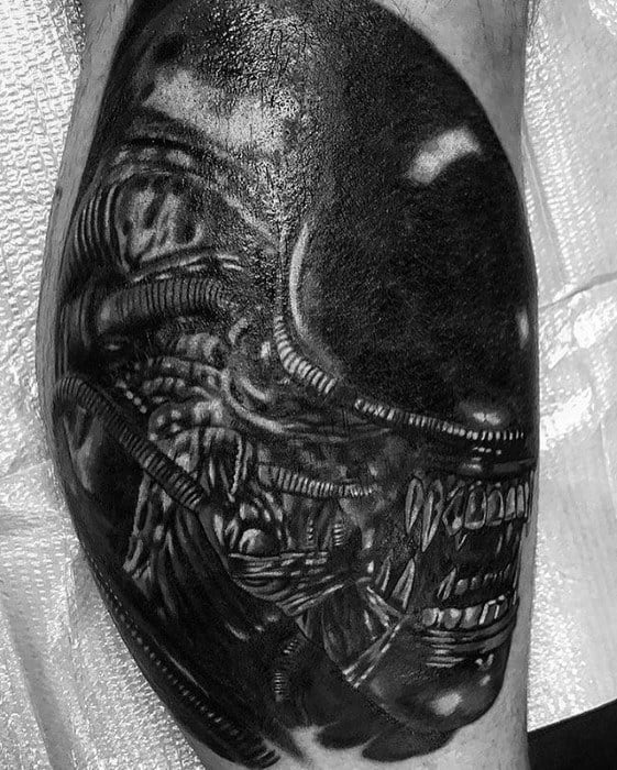 Hyper-realistic black and grey Xenomorph tattoo showing a close-up of the creature’s snarling face and detailed biomechanical textures.