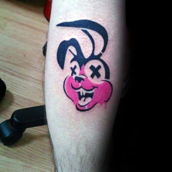 Tattoo of a mischievous cartoon bunny with pink cheeks and X eyes, echoing Green Day’s punk-inspired logo style.