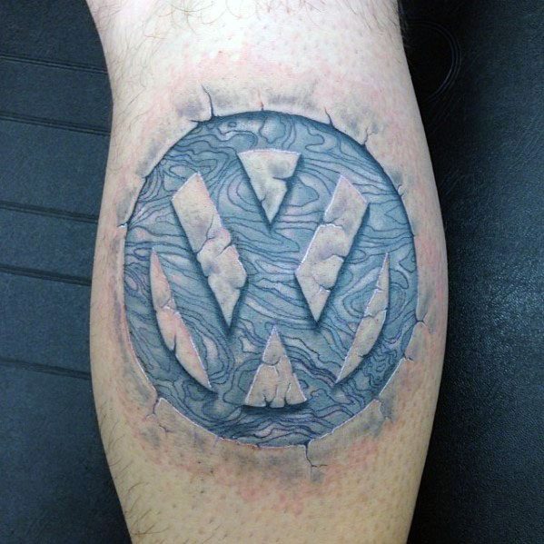 Volkswagen logo tattoo with a stone-like texture and cracked 3D effect, making it appear carved into the skin.