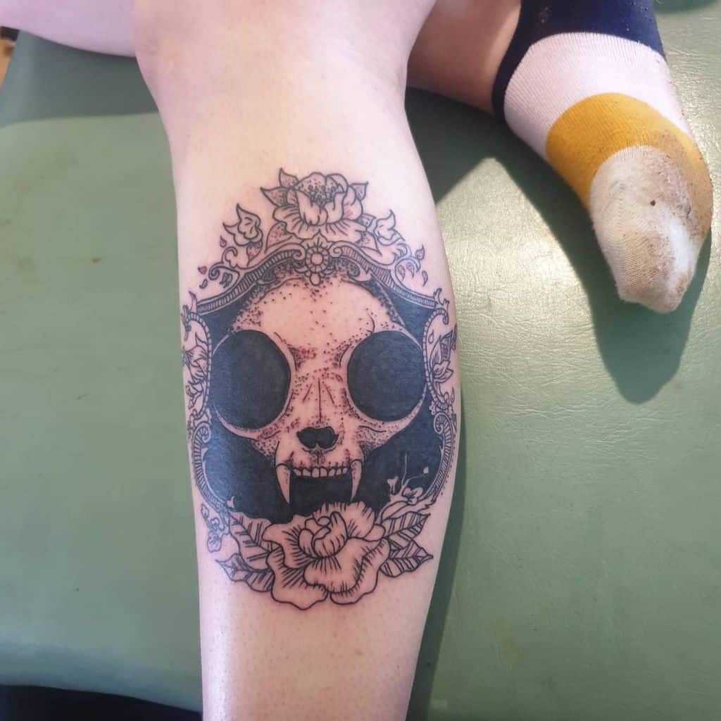 Leg tattoo featuring an ornate cat skull design with roses and decorative elements