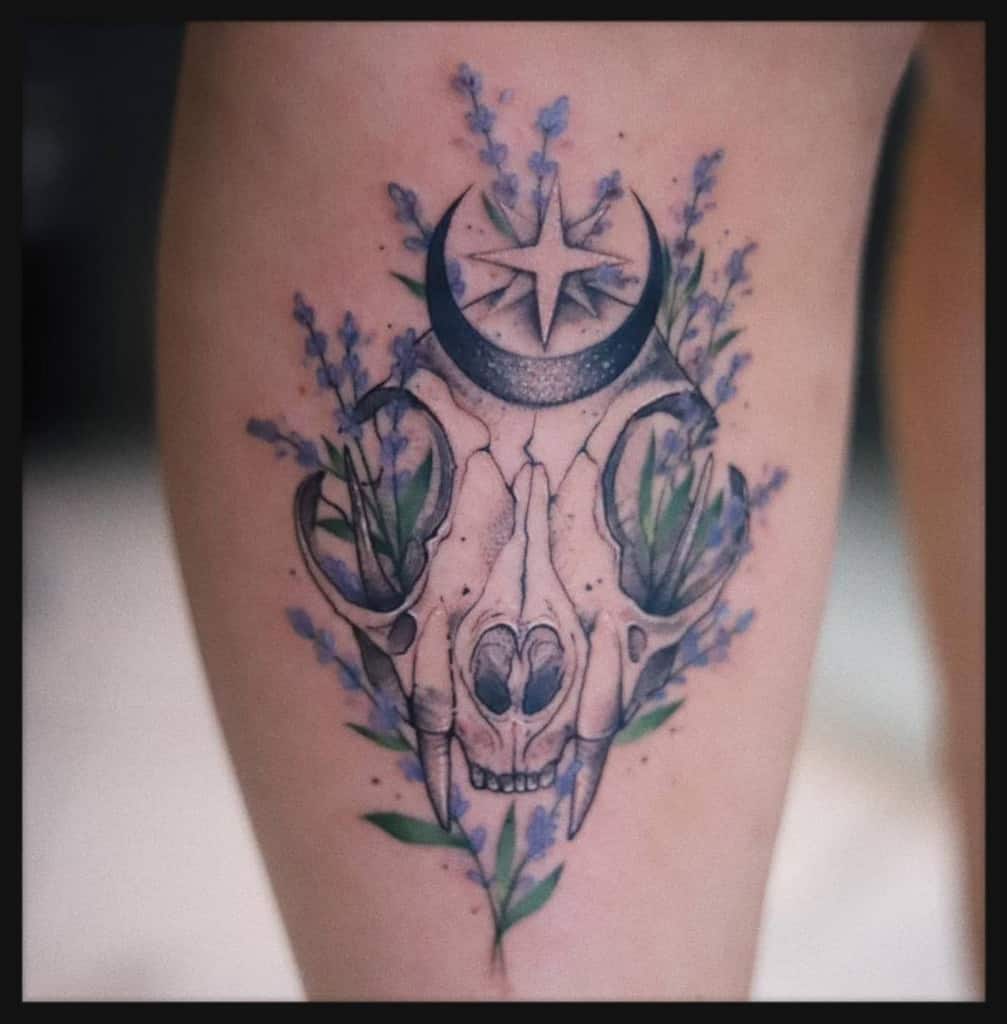 Tattoo of a cat skull with flowers, a crescent moon, and a star on a leg