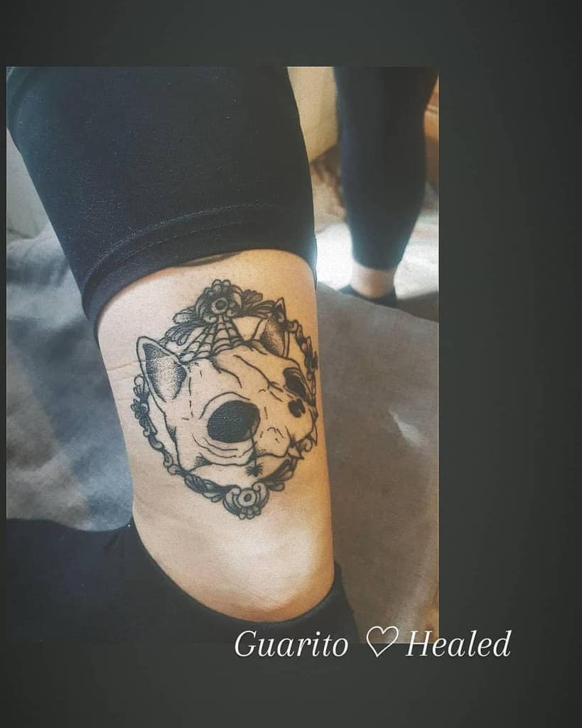 Tattoo of a cat skull inside an ornate frame on the back of a leg