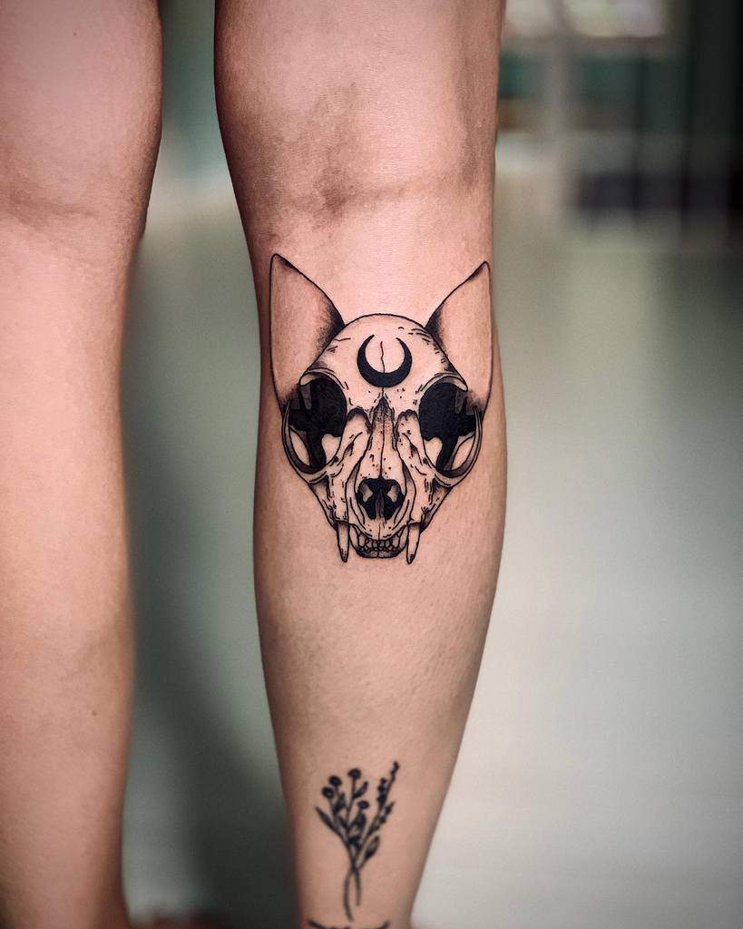 Tattoo of a cat skull intertwined with a crescent moon adorns a person's calf