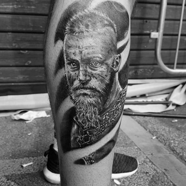 Black and white leg tattoo depicting a detailed, bearded man with intense gaze and warrior attire