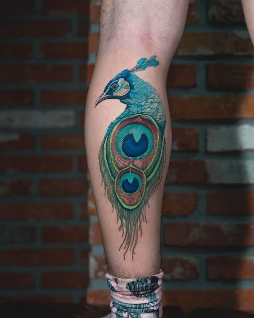 Vibrant peacock tattoo with colorful tail feathers in blue, green, and yellow, elegantly placed on the calf.