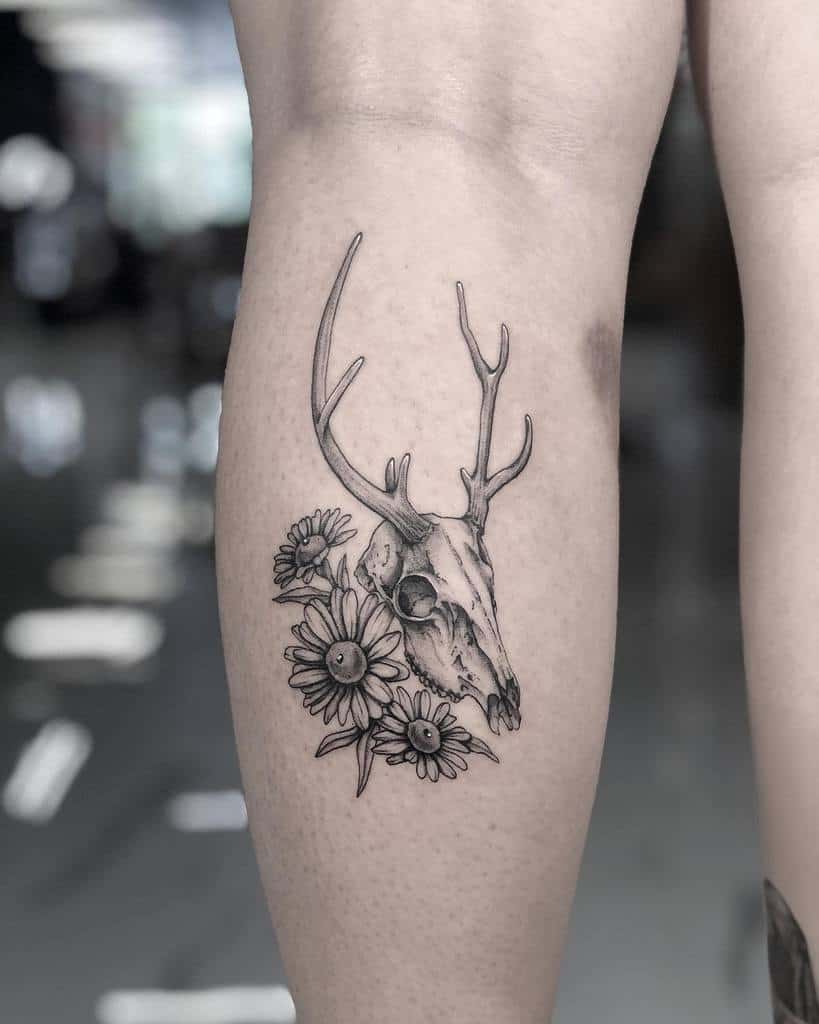 Tattoo of a deer skull with antlers and sunflowers on a person's calf, capturing the beauty of nature's cycle