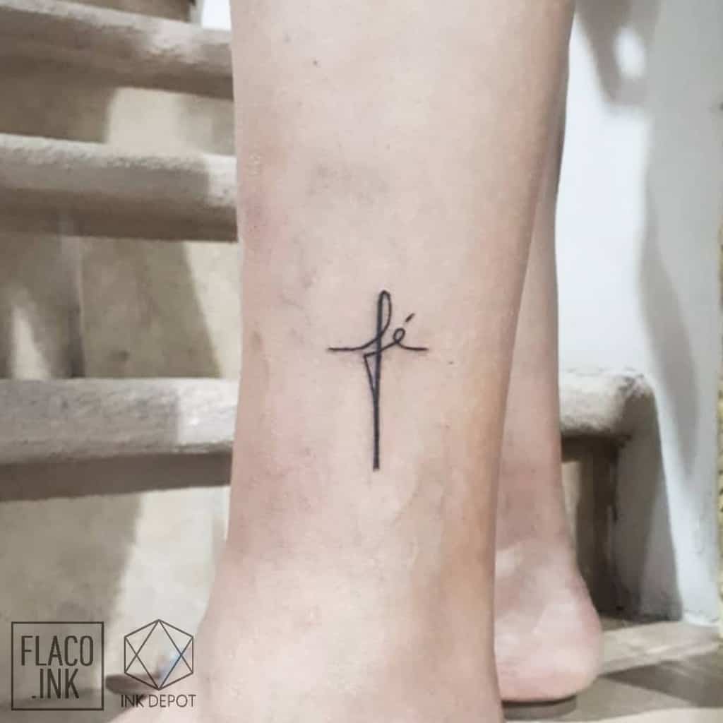 A delicate ankle tattoo featuring a cross elegantly entwined with the word “fé,” symbolizing profound faith
