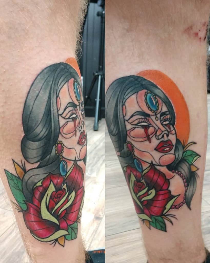 Colorful tattoo of a stylized gypsy woman adorned with jewelry and a rose on a leg