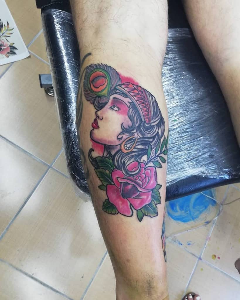 Vivid tattoo of a gypsy woman adorned with a peacock feather and roses on a calf