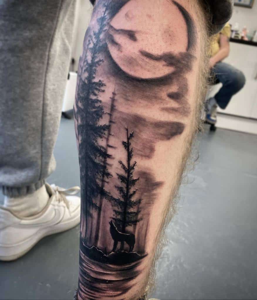Tattoo of a forest scene with a wolf howling under a full moon on a leg
