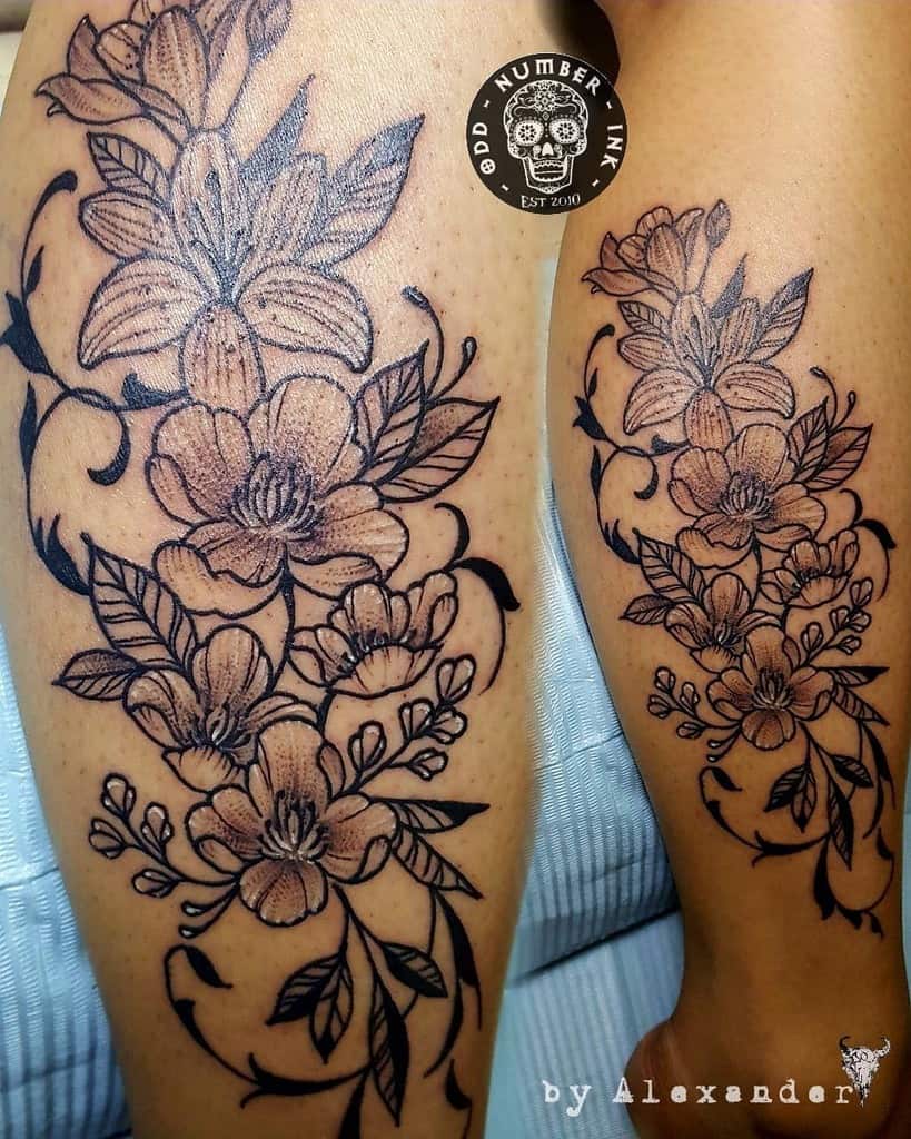 Two tattooed legs featuring intricate floral designs with leaves and blossoms