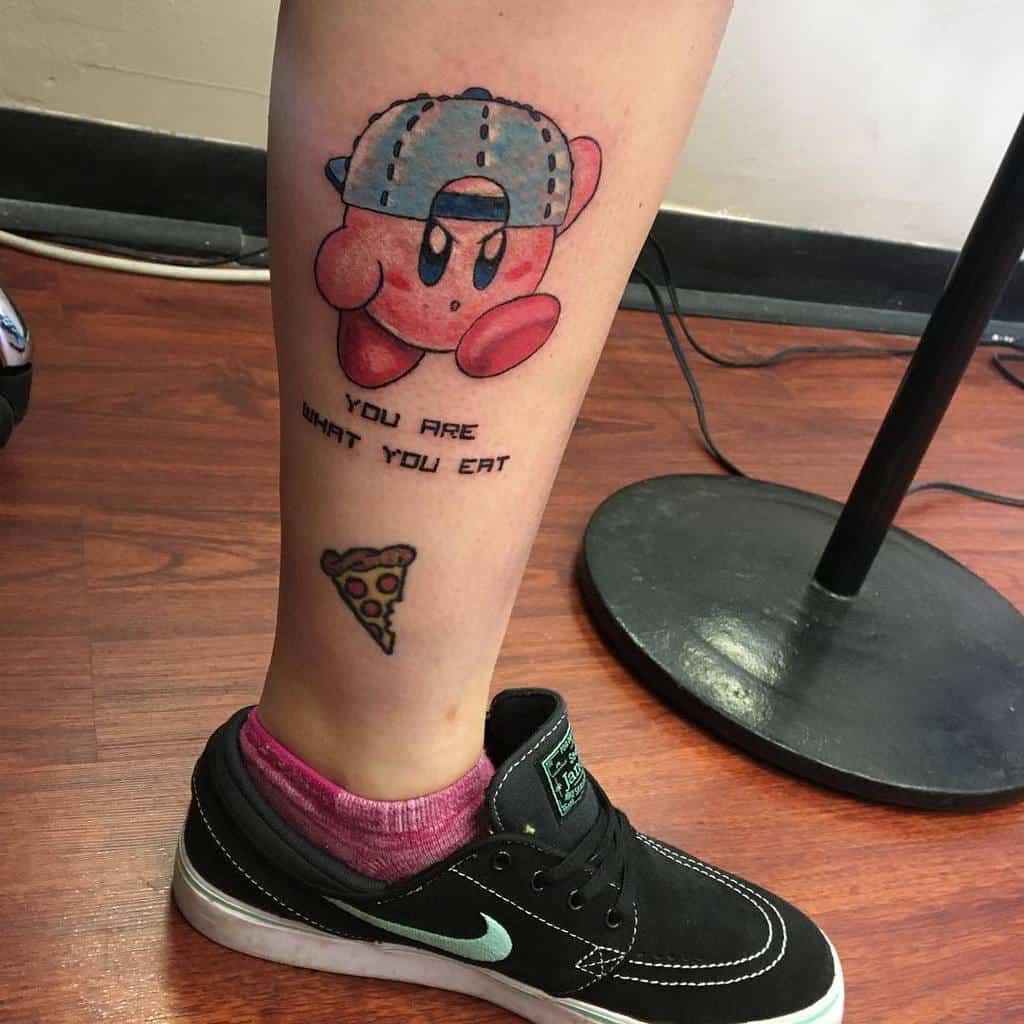 Kirby tattoo wearing a backward cap, next to the phrase "YOU ARE WHAT YOU EAT" and a slice of pizza
