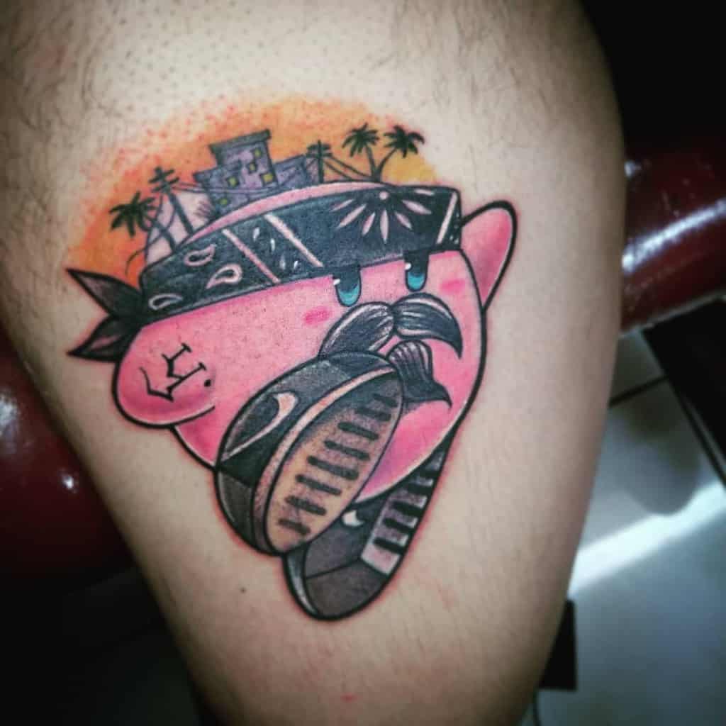 Kirby tattoo with a gangster-style design, wearing a bandana, mustache, and holding a sneaker, with a cityscape and palm trees in the background