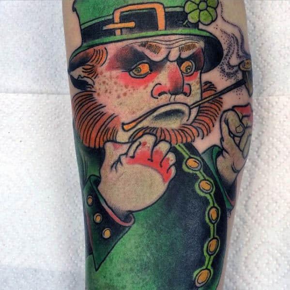 Bold tattoo of a grumpy leprechaun in a green coat and clover hat, clenching his fists with a pipe in his mouth and flushed cheeks.