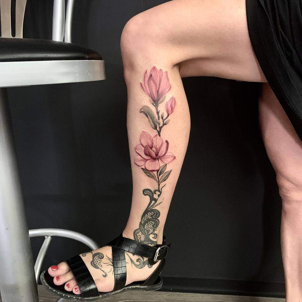 The tattoo features a beautiful magnolia flower design on the leg, with vibrant pink hues and delicate shading that create a soft, realistic look