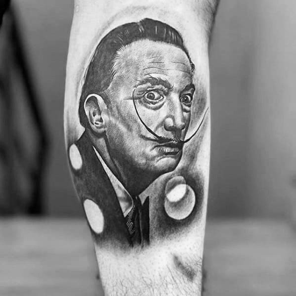 Black and grey Salvador Dali tattoo with a sharp portrait style, surreal floating spheres, and dramatic contrast for a timeless surrealist vibe.