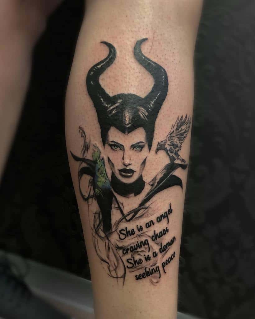 A bold leg tattoo featuring Maleficent with striking horns and dramatic shading. Complemented by a poetic quote, 'She is an angel craving chaos. She is a demon seeking peace,' and delicate details of her iconic raven and green aura
