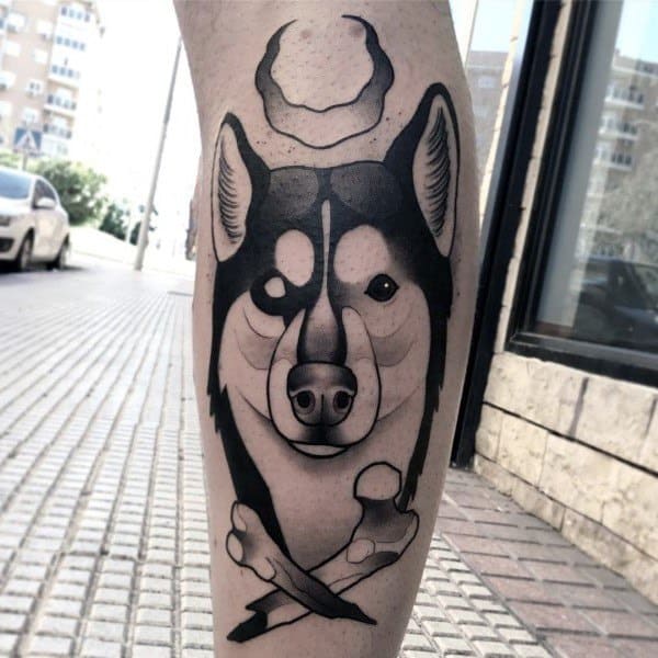 Bold blackwork Siberian Husky tattoo on a man's leg, featuring strong lines, geometric elements, and a crossed bone design for a striking look.