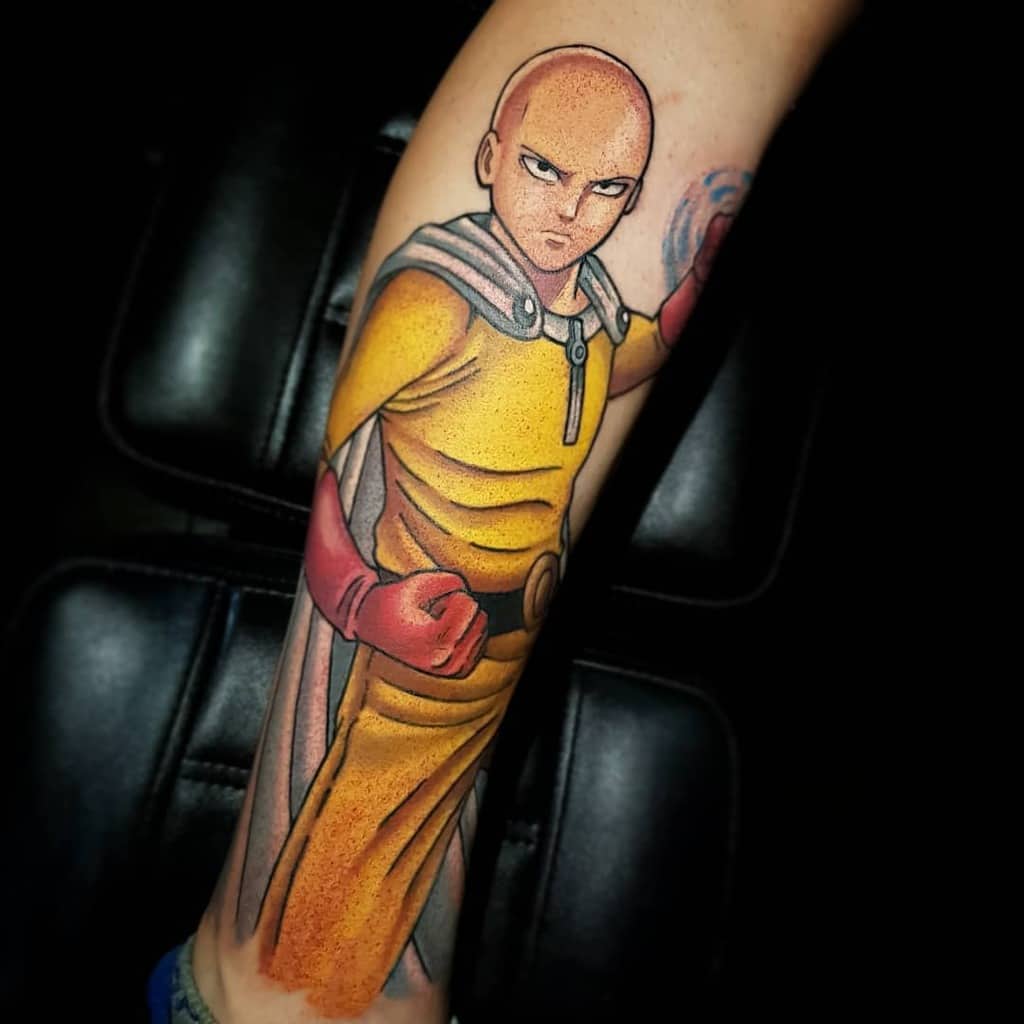 A bold and vibrant tattoo of Saitama from One Punch Man in his yellow suit, red gloves, and cape, striking a powerful stance on the leg