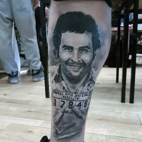 Detailed black and gray tattoo of Pablo Escobar, featuring his mugshot with Medellín Judicial branding and bullet imagery below