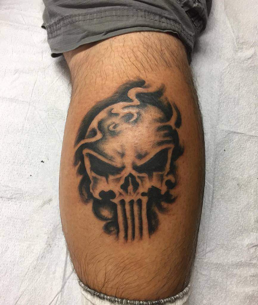 A leg with a dark Punisher Skull tattoo featuring flames on its head