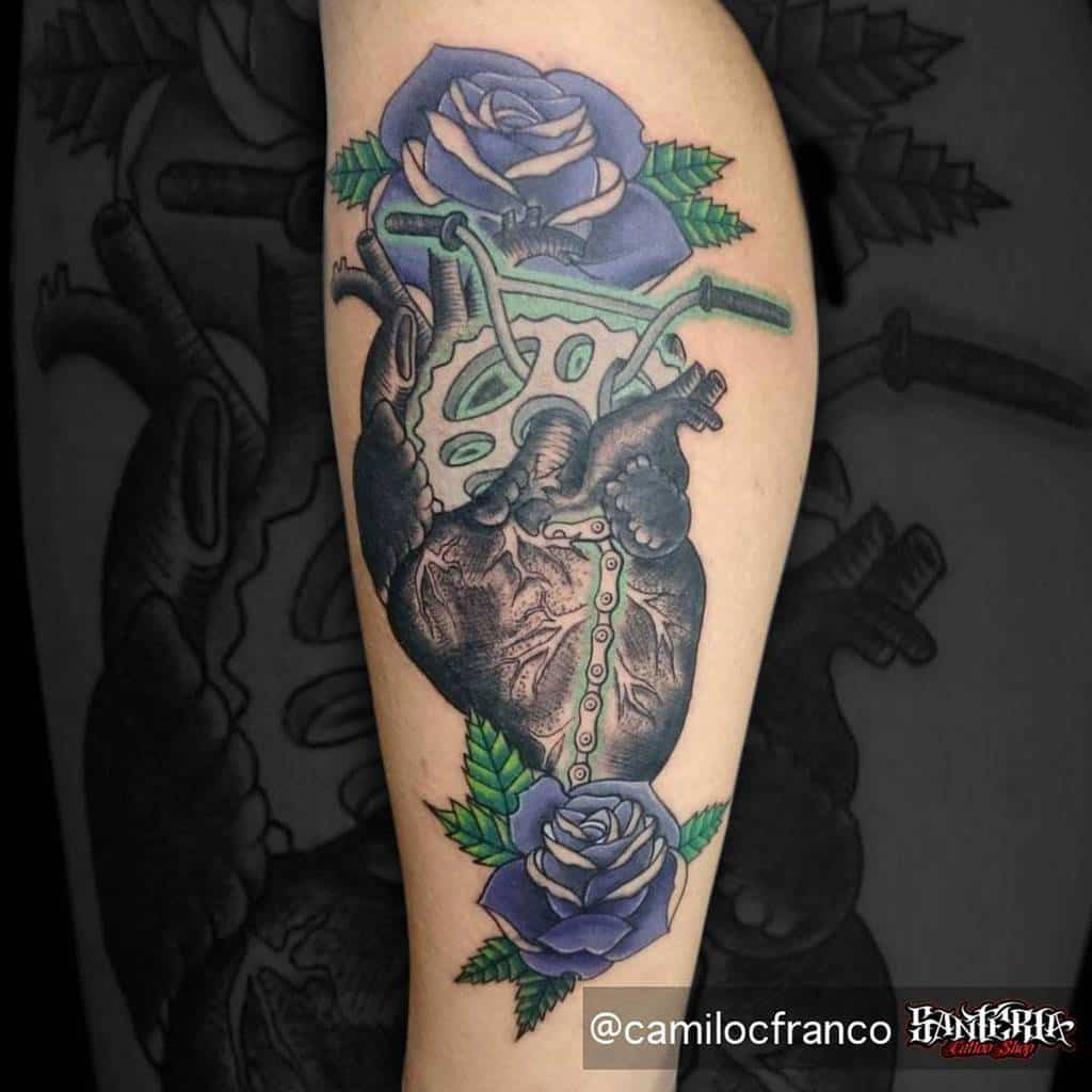 A tattoo of a realistic anatomical heart adorned with purple roses, intertwined with lush green leaves