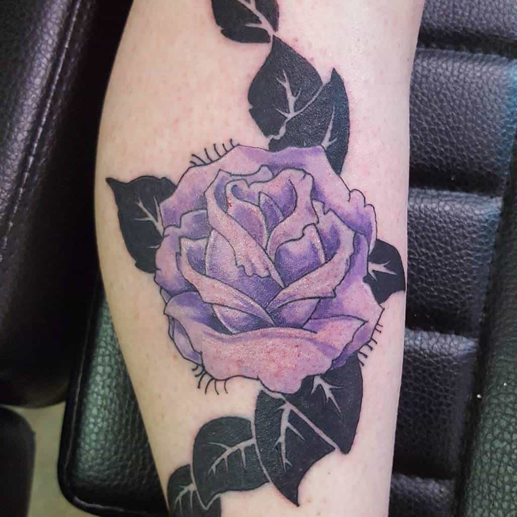 Tattoo of a purple rose with dark leaves on a leg
