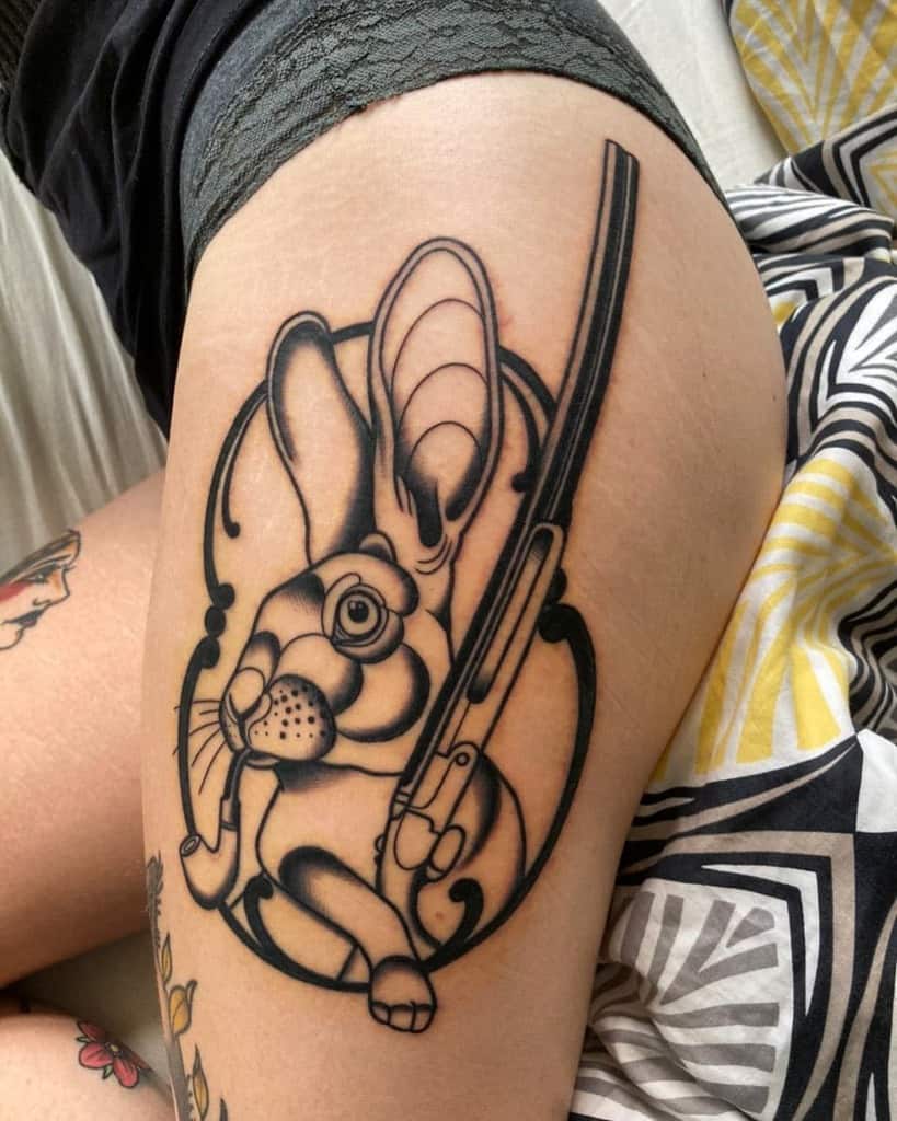 Bold black line tattoo of a rabbit holding a gun, framed within a rabbit design