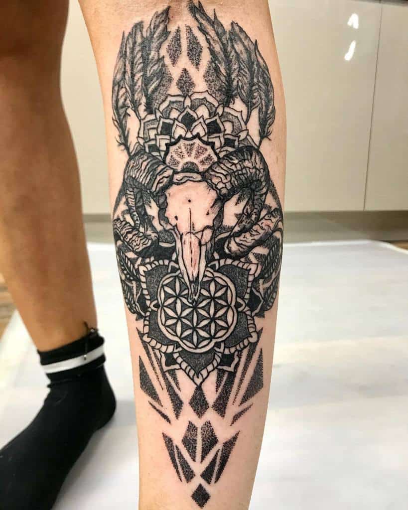 Intricate tattoo featuring a ram skull intertwined with floral and geometric designs on a calf