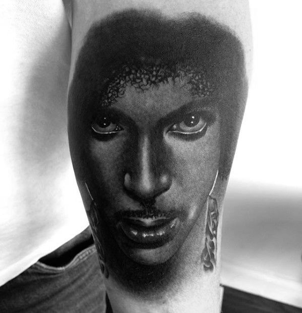 An intense black-and-gray tattoo of Prince's face, capturing his piercing gaze and iconic features