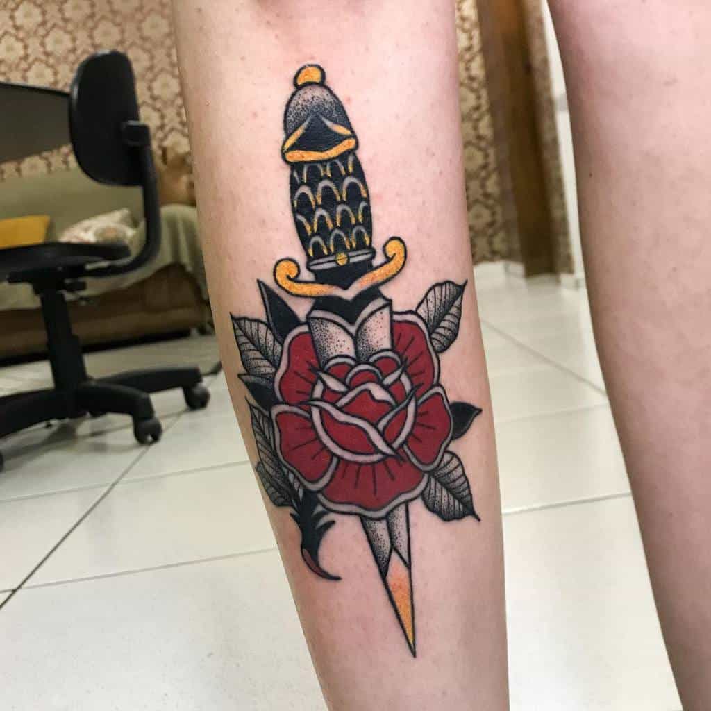 Tattoo of a dagger piercing a red rose with dark leaves on a calf