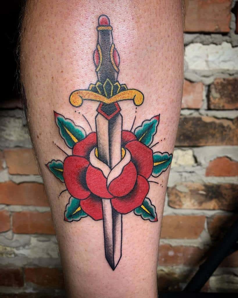 Tattoo of a dagger piercing a red rose with green leaves on a leg