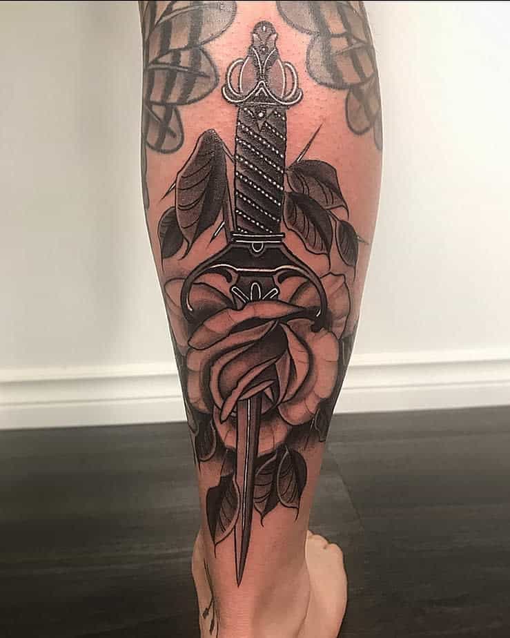 A tattoo of a dagger through a rose inked on the back of a calf