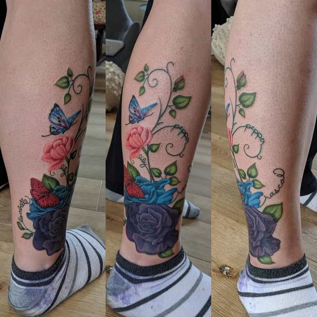 Colorful leg tattoo featuring roses in pink, blue, and purple hues, intertwined with green vines and butterflies for a vibrant, dynamic design