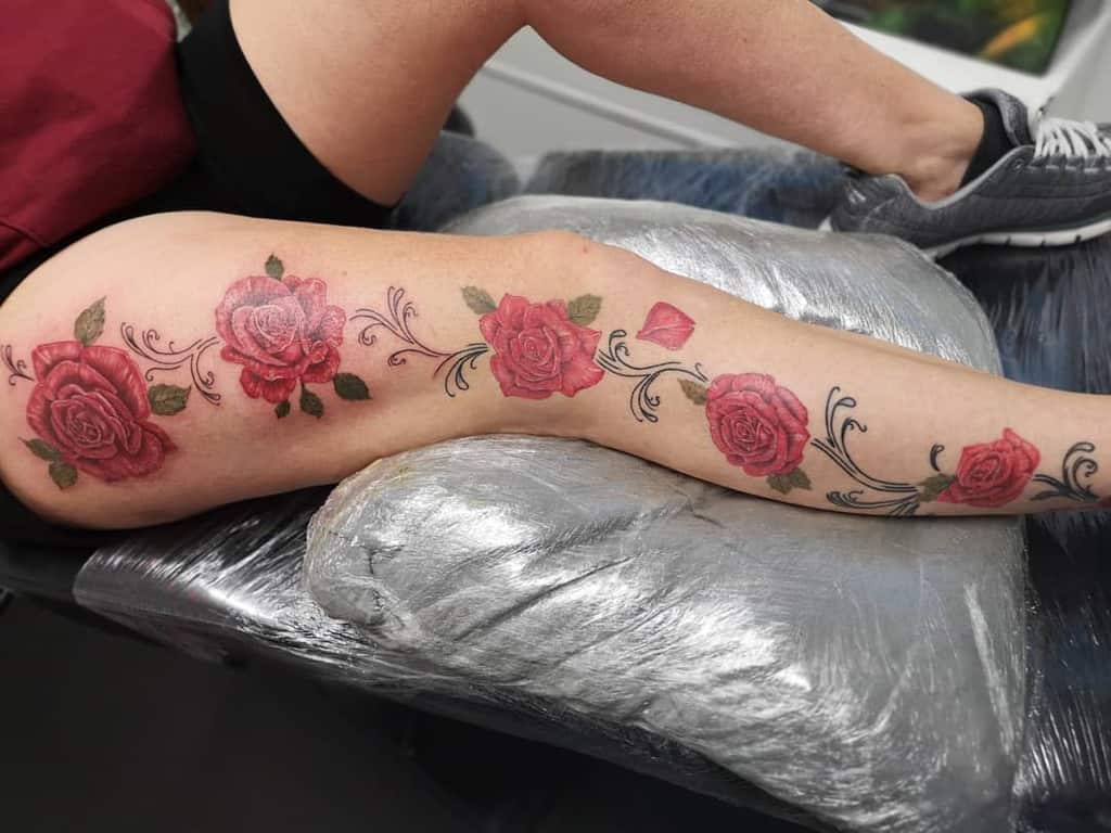 Elegant leg tattoo featuring a series of red roses connected by swirling black vines and delicate green leaves for a cohesive floral design