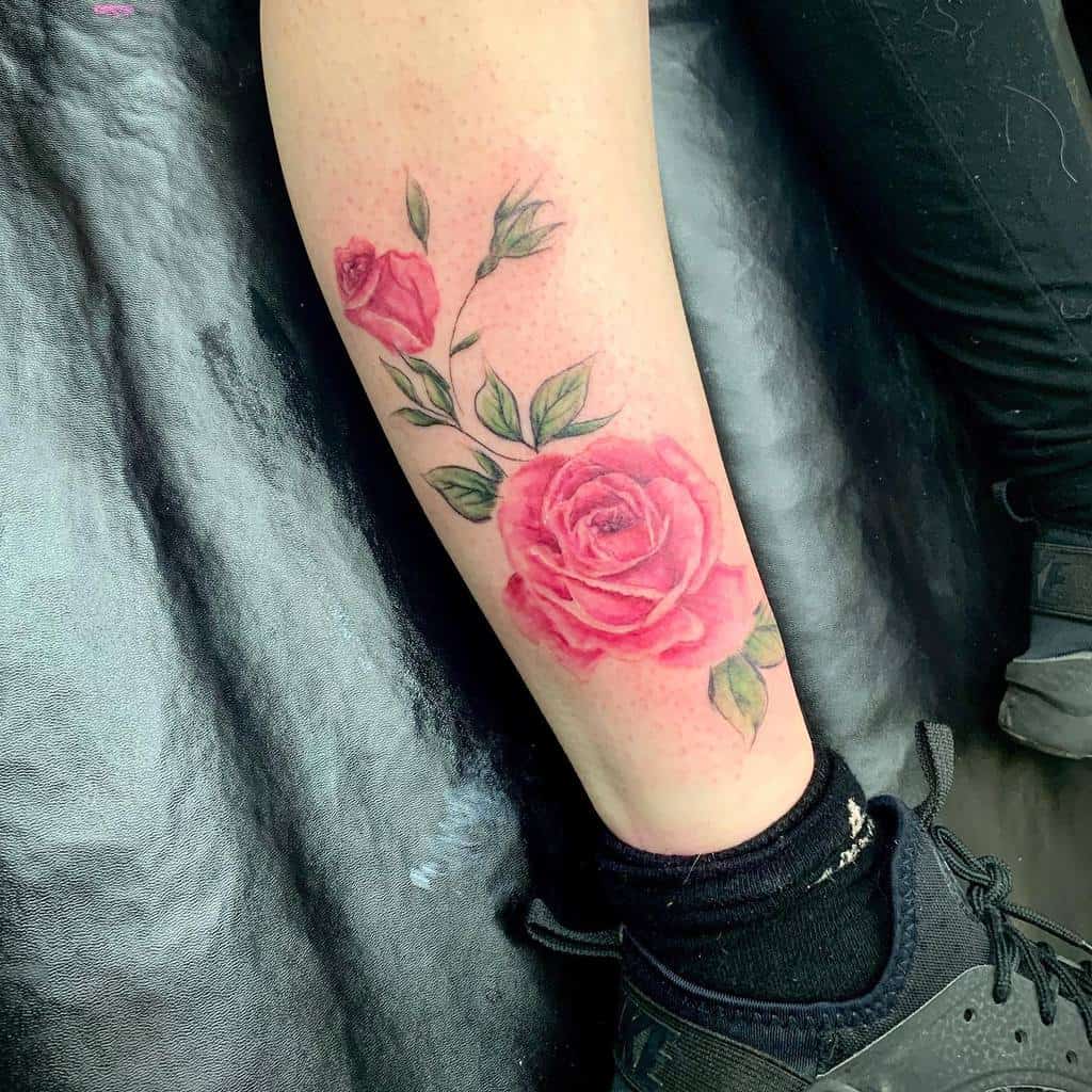 Delicate leg tattoo showcasing a vibrant pink rose with smaller buds and green leaves, creating a soft and elegant floral design