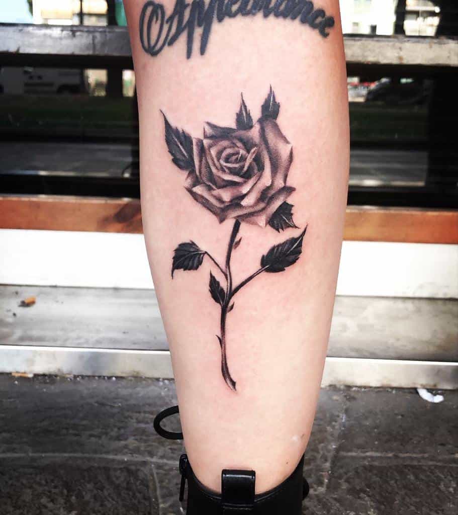 A striking black rose tattoo adorns the leg, complete with an elegant stem that leads gracefully to cursive lettering above