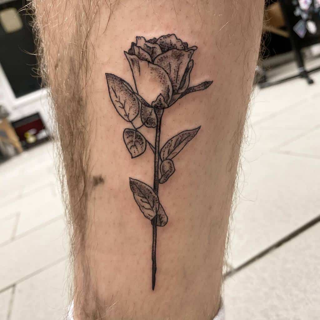 A black and white rose tattoo elegantly winds around a leg, its intricate stem adding depth and artistry