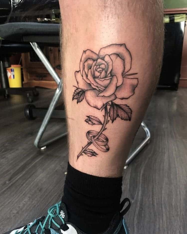 A leg tattoo featuring a detailed rose with intricate leaves and a beautifully winding stem