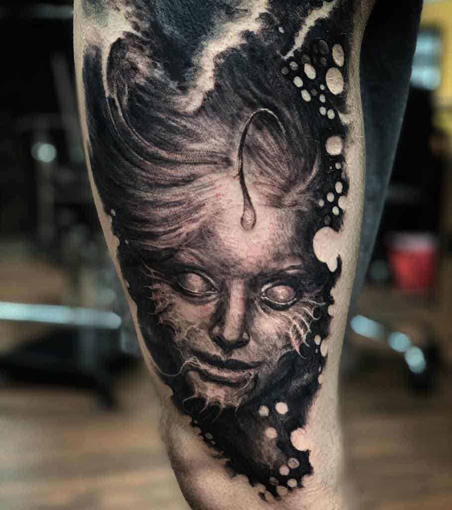 Dark, surreal leg tattoo of a siren's haunting face, surrounded by flowing hair and abstract underwater elements