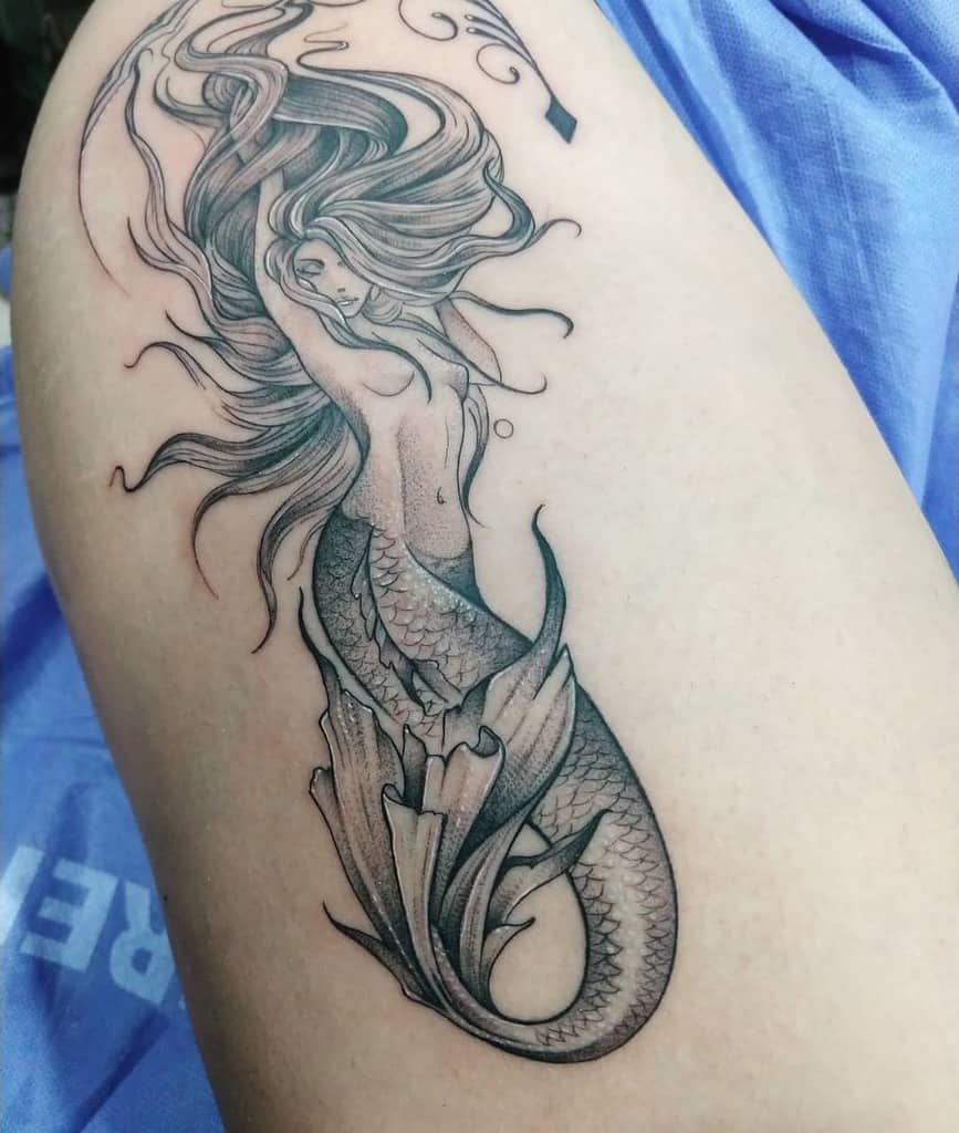 Elegant black and grey tattoo of a mermaid with flowing hair, delicate shading, and intricate scale details