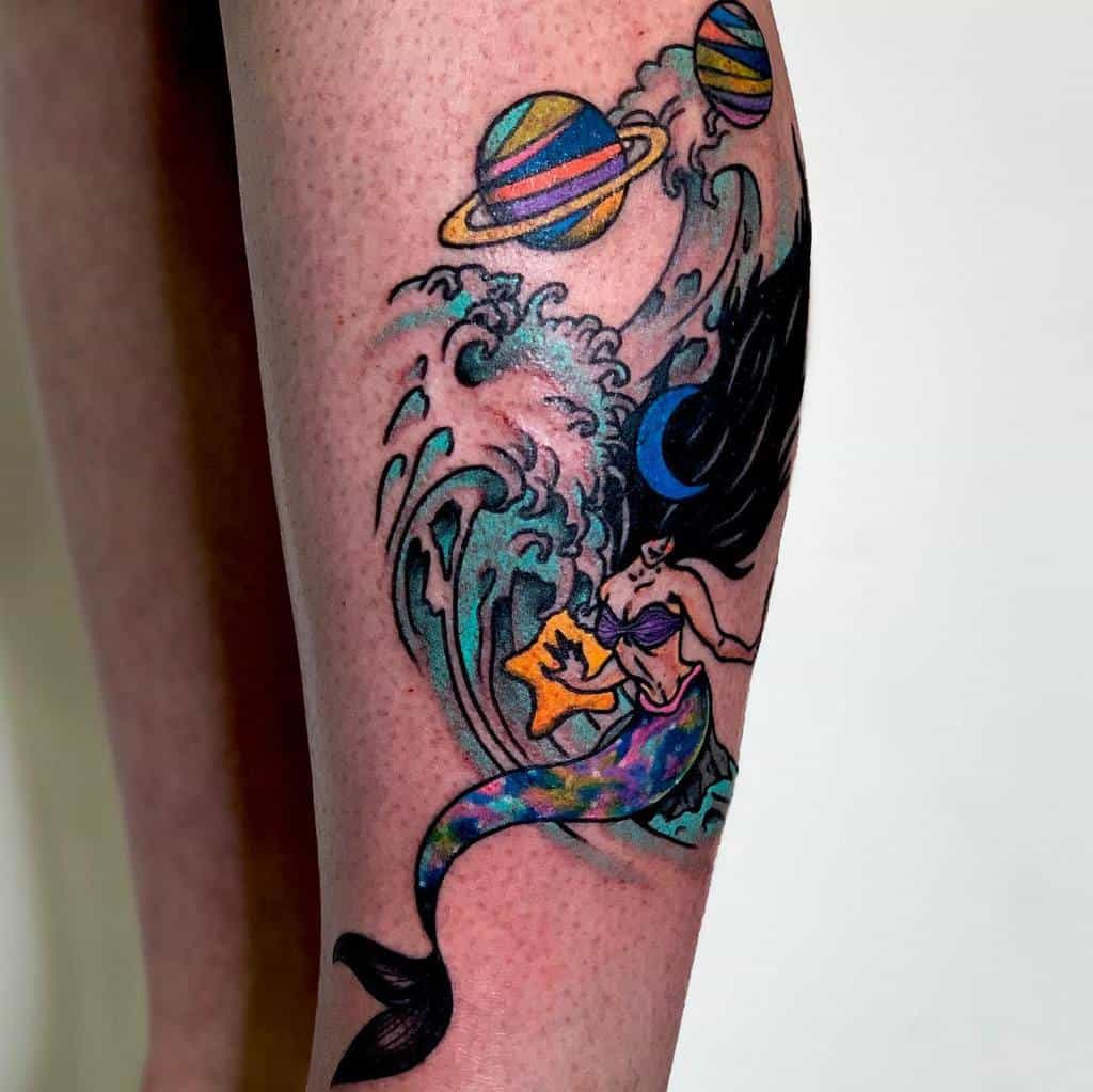 Vibrant tattoo of a cosmic mermaid with a colorful tail, crashing waves, and planets in the background, blending ocean and space themes