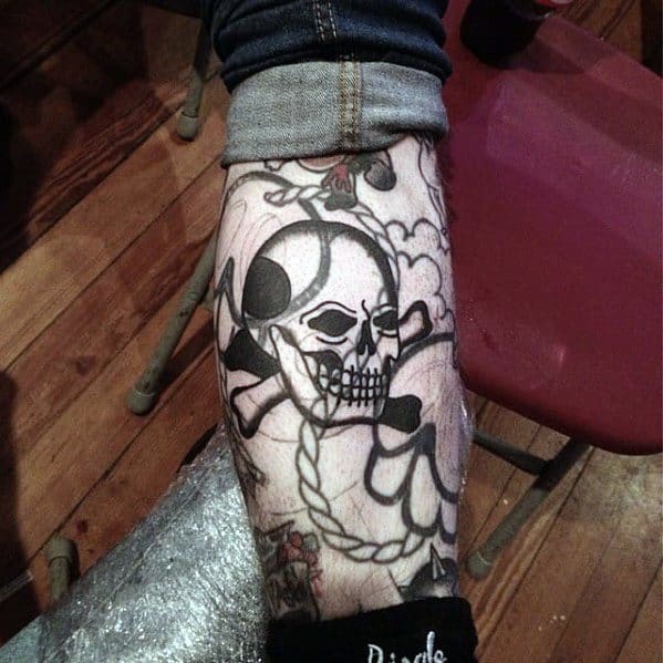 Blast-over leg tattoo featuring a skull and crossbones with floral accents