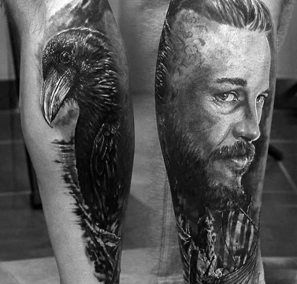Black and white tattoos of a raven and a man's portrait on two separate legs