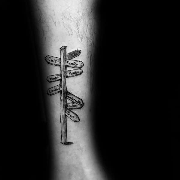 Minimalist black and grey tattoo of a wooden signpost with directional signs labeled 'Family,' 'Passion,' 'Honor,' 'Creativity,' and more.
