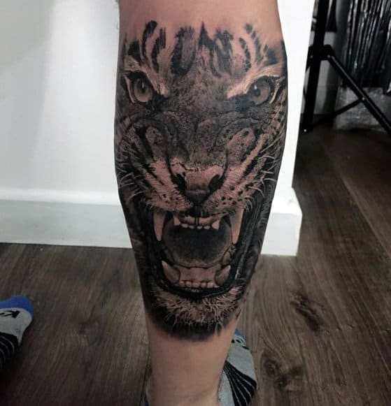 Leg tattoo of a roaring tiger head with detailed fur and fierce eyes