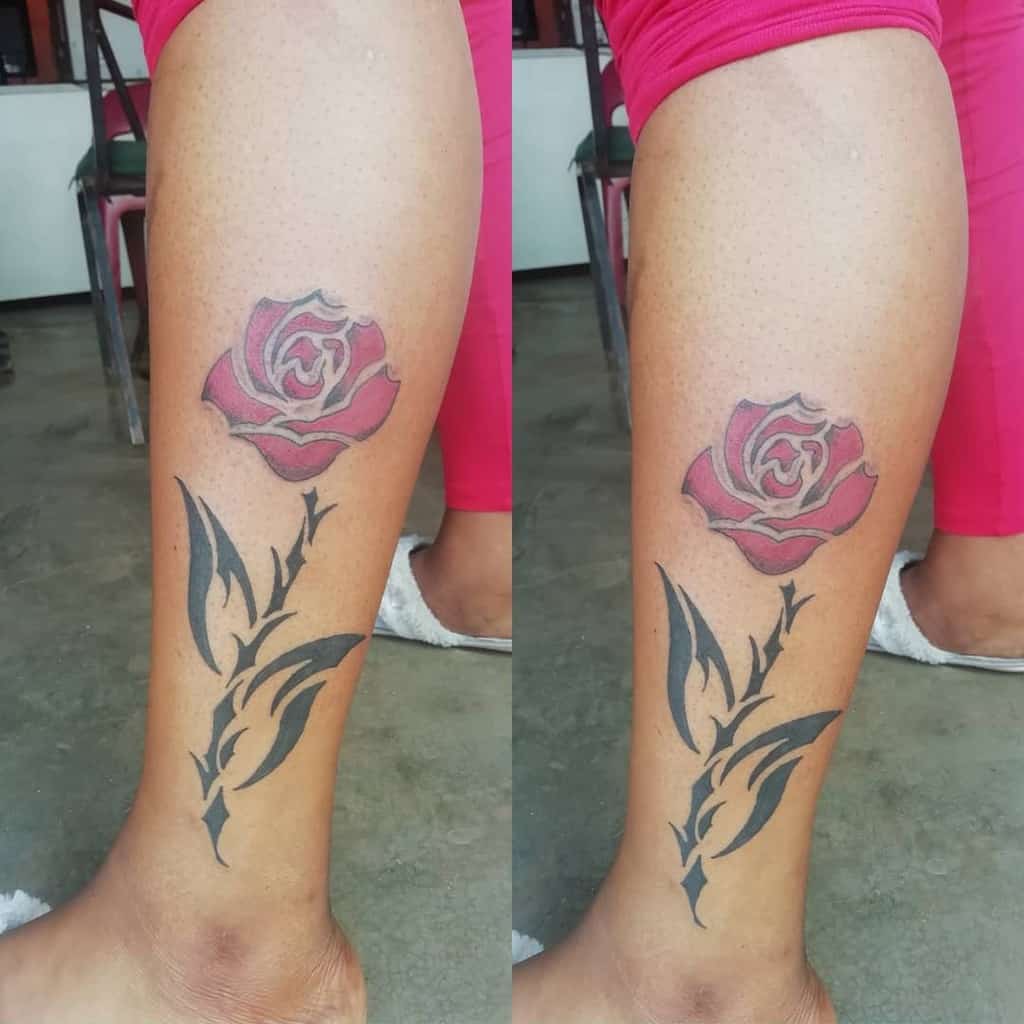 A striking tattoo of a red rose with black leaves elegantly entwined in a tribal design on a person's calf