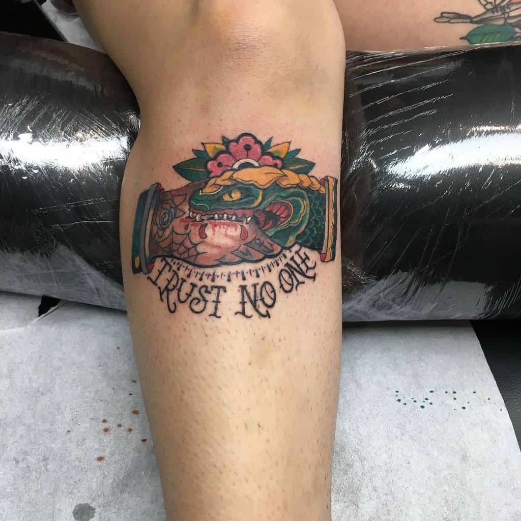 Leg tattoo featuring a snake coiled around a hand, adorned with a vibrant flower at the top, with the words 'Trust no one' in stylized lettering beneath the design